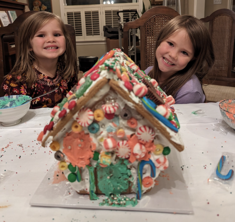 Me and my sister posing behind a gingerbread house covered in candy.